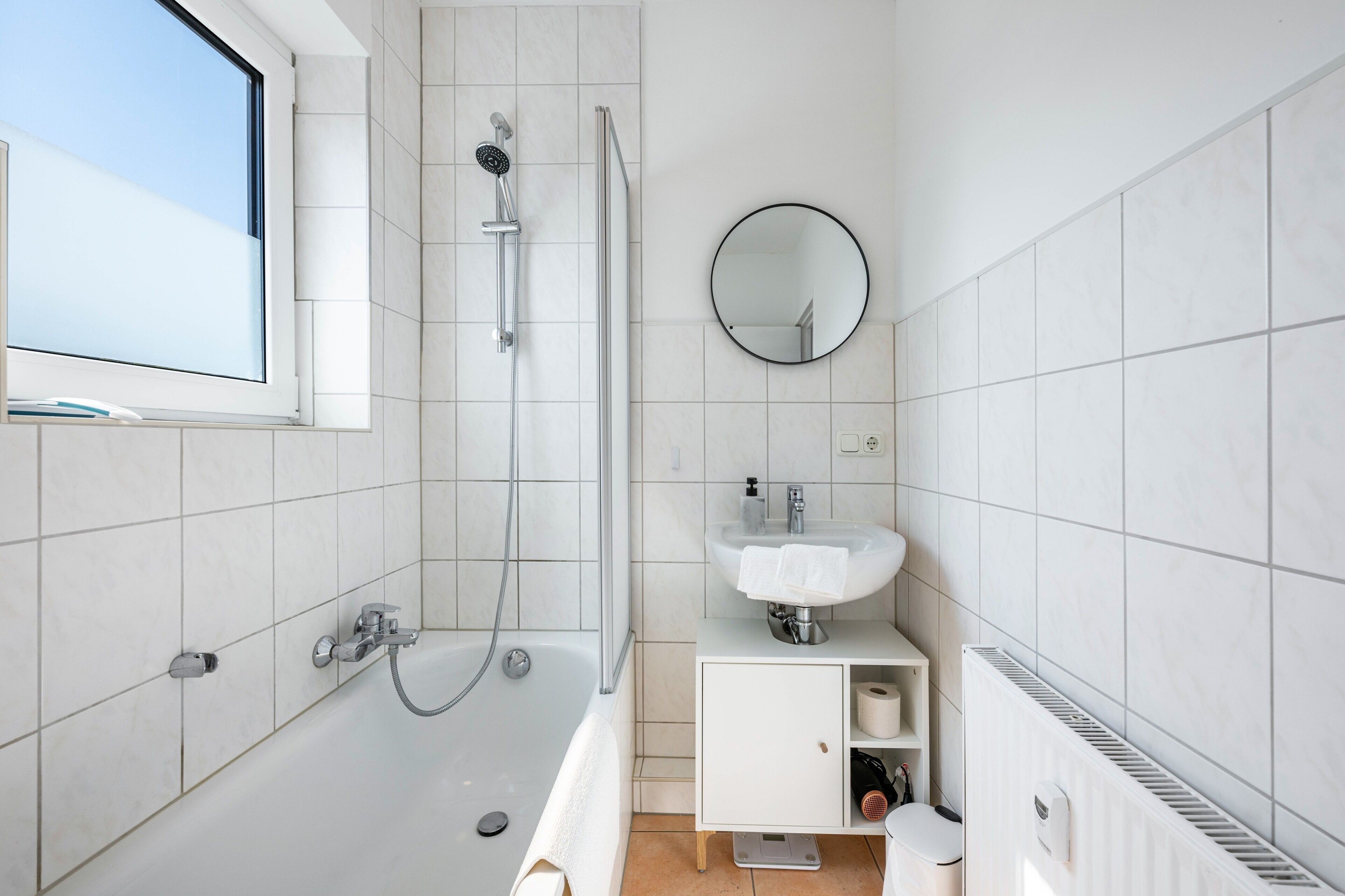 A modern bathroom with a bathtub, shower, sink, and a window.