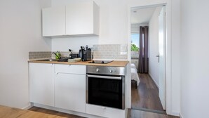 A compact kitchen with white cabinets, a wooden countertop, a built-in oven, and a view into a bedroom through an open door. - Apartment 'Mit Dachterrasse' with Lake View, Balcony and Wi-Fi (Heide)