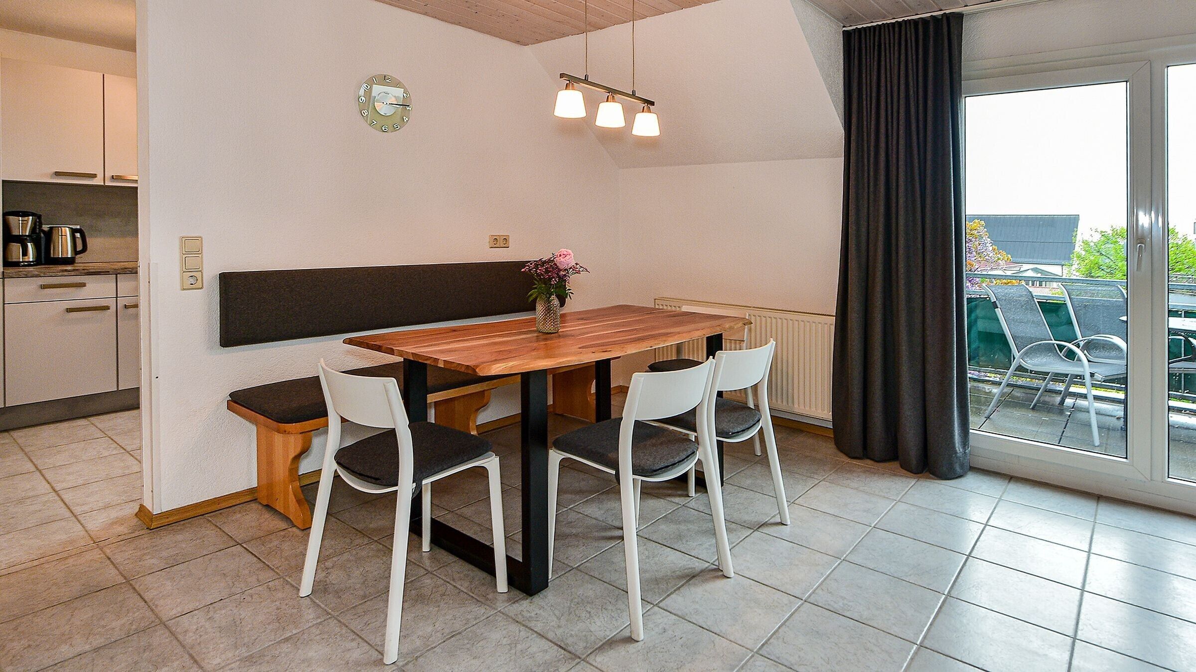 Una cocina moderna con una mesa de madera y sillas blancas, un reloj y vistas al exterior.