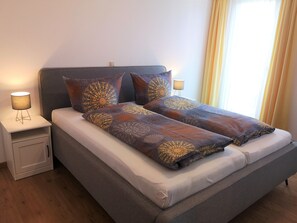 A double bed with patterned bedding, bedside lamps, a nightstand, and a window with curtains. - Apartment '5' with Lake View, Shared Terrace and Wi-Fi (Lindau am Bodensee)