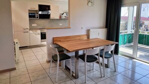 Une cuisine moderne dotée d’un four et d’un micro-ondes encastrés, d’une table à manger en bois avec quatre chaises, et d’une porte-fenêtre coulissante donnant sur un balcon.