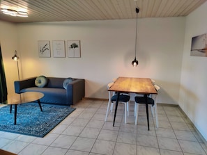 A room with a wooden ceiling, a dining table with chairs, a sofa with cushions, and wall art. - Apartment '1' with Shared Terrace, Shared Garden and Wi-Fi (Lindau am Bodensee)