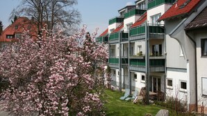 A multi-story residential building with balconies, a garden area with pink flowering trees, and a clear sky. - Apartment '1' with Shared Terrace, Shared Garden and Wi-Fi (Lindau am Bodensee)
