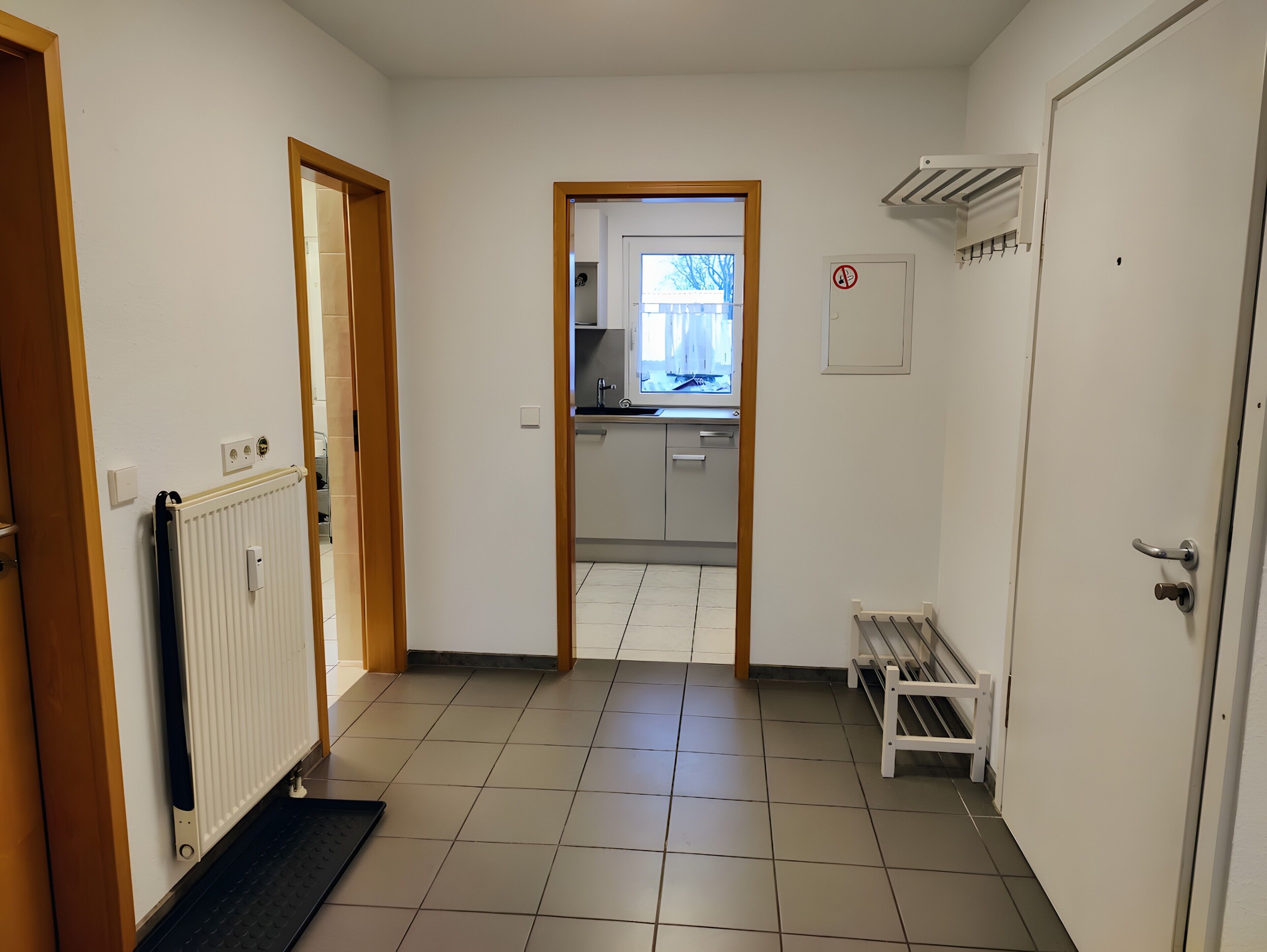 A hallway with a radiator, a bench, a door, and a view into a kitchen area.