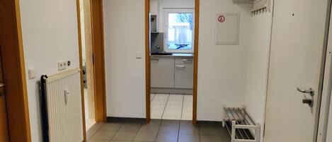 A hallway with a radiator, a bench, a door, and a view into a kitchen area.