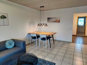 Een moderne woonkamer met een houten eettafel, twee stoelen, een bank en een salontafel.
