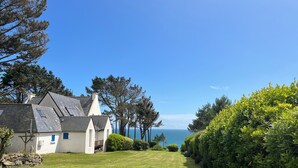A coastal house with a grassy lawn, a stone wall, and a view of the sea.