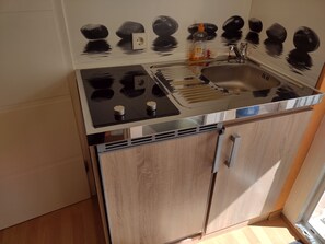 Een koelkast, een kookplaat, een waterkoker, kookgerei, borden en bestek