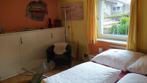 A bedroom with a bed, a chair, a glass table, a wardrobe, and a window with a view of greenery outside. - Holiday Apartment '19sqm' with Wi-Fi in Quiet St. Georgen Backyard (Freiburg)