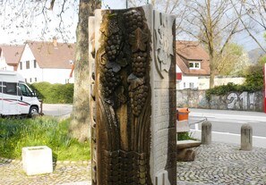 Ein Steinsockel mit aufwendigen Schnitzereien, ein Kopfsteinpflasterweg und ein weißer Van in der Nähe.
