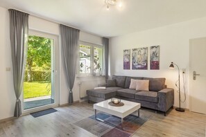 A modern living room with a sectional sofa, a coffee table, and a large window with curtains. - Apartment 'Rastplatz' with Mountain View, Private Terrace and Wi-Fi (Schmallenberg)
