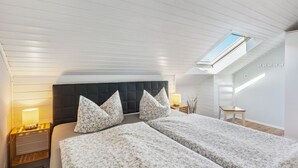 Un dormitorio con dos camas, un tragaluz, una mesita de noche con lámpara y una silla de madera.