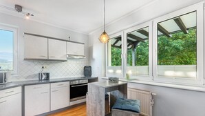 Una cocina moderna con armarios blancos, horno empotrado, encimera de madera y ventana con vistas a zonas verdes.