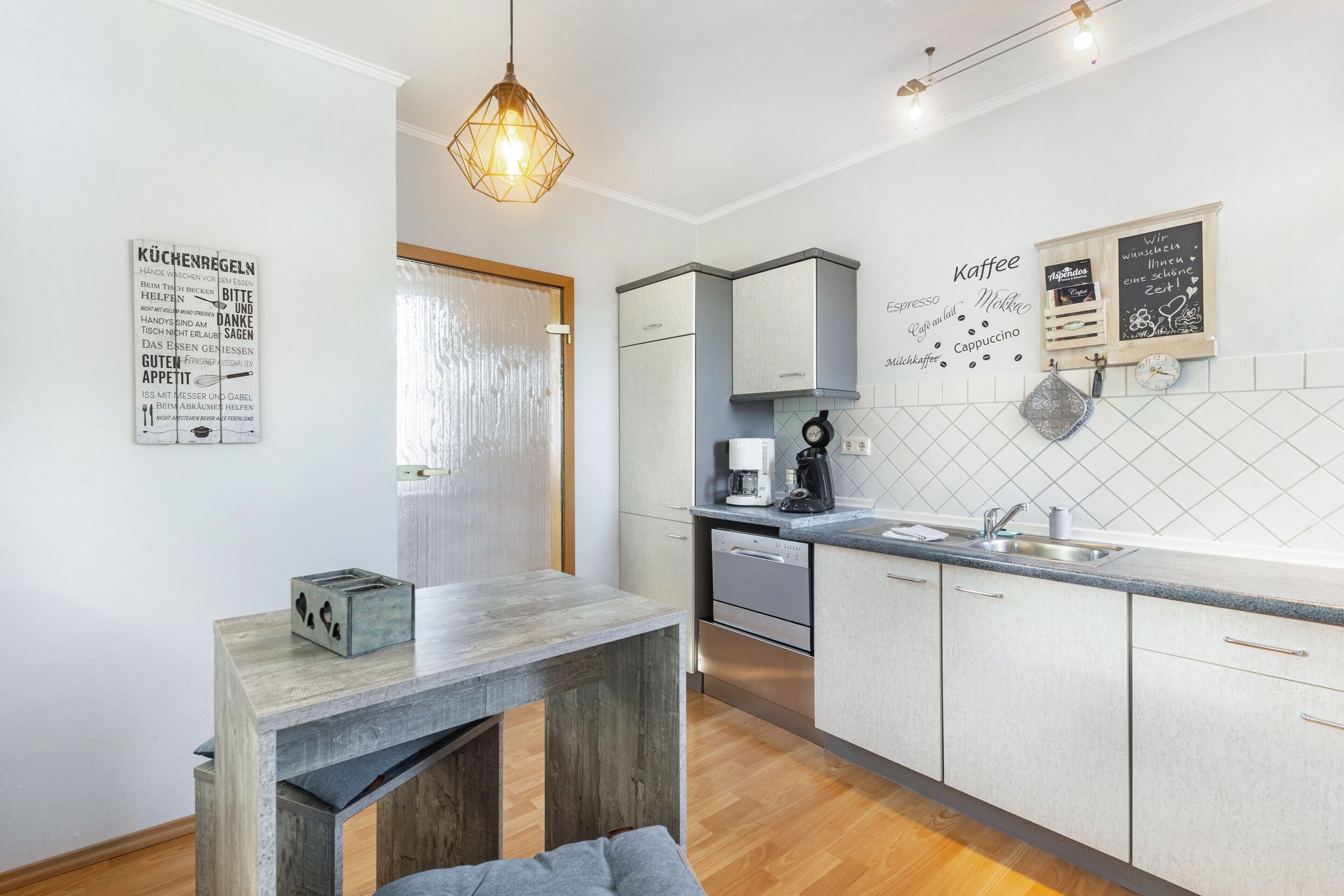 A modern kitchen with a wooden table, a coffee machine, and a chalkboard menu.