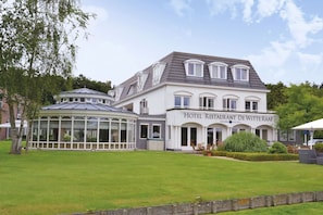 Experience the charm of Hotel Restaurant De Witte Raaf, a classic building with a symmetrical facade, large windows, and a glass conservatory.
