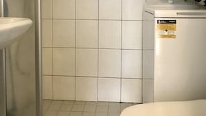 Un baño con azulejos blancos, un lavamanos blanco, un inodoro y una zona de ducha.
