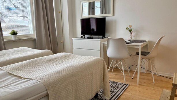 Una habitación de hotel con dos camas, un escritorio con ordenador, televisión y ventana con cortinas.