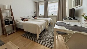 Habitación de hotel con dos camas, un escritorio con computadora, televisor, escalera y ventana con cortinas.