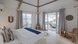 A spacious bedroom with a large bed, wooden beams on the ceiling, and a view of the outdoors through large windows. - Villa Cocodrilos 2 by Pertama Stay (Seminyak)