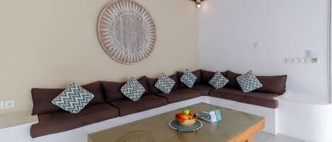 A modern living room with a brown sectional sofa, a glass coffee table with fruits, and a decorative wall piece.