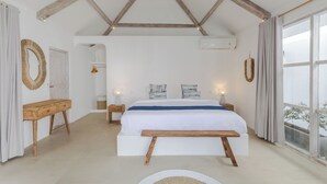 A bedroom with a large bed, wooden beams on the ceiling, a window with a view, and a bedside table with a lamp. - Villa Cocodrilos 2 by Pertama Stay (Seminyak)