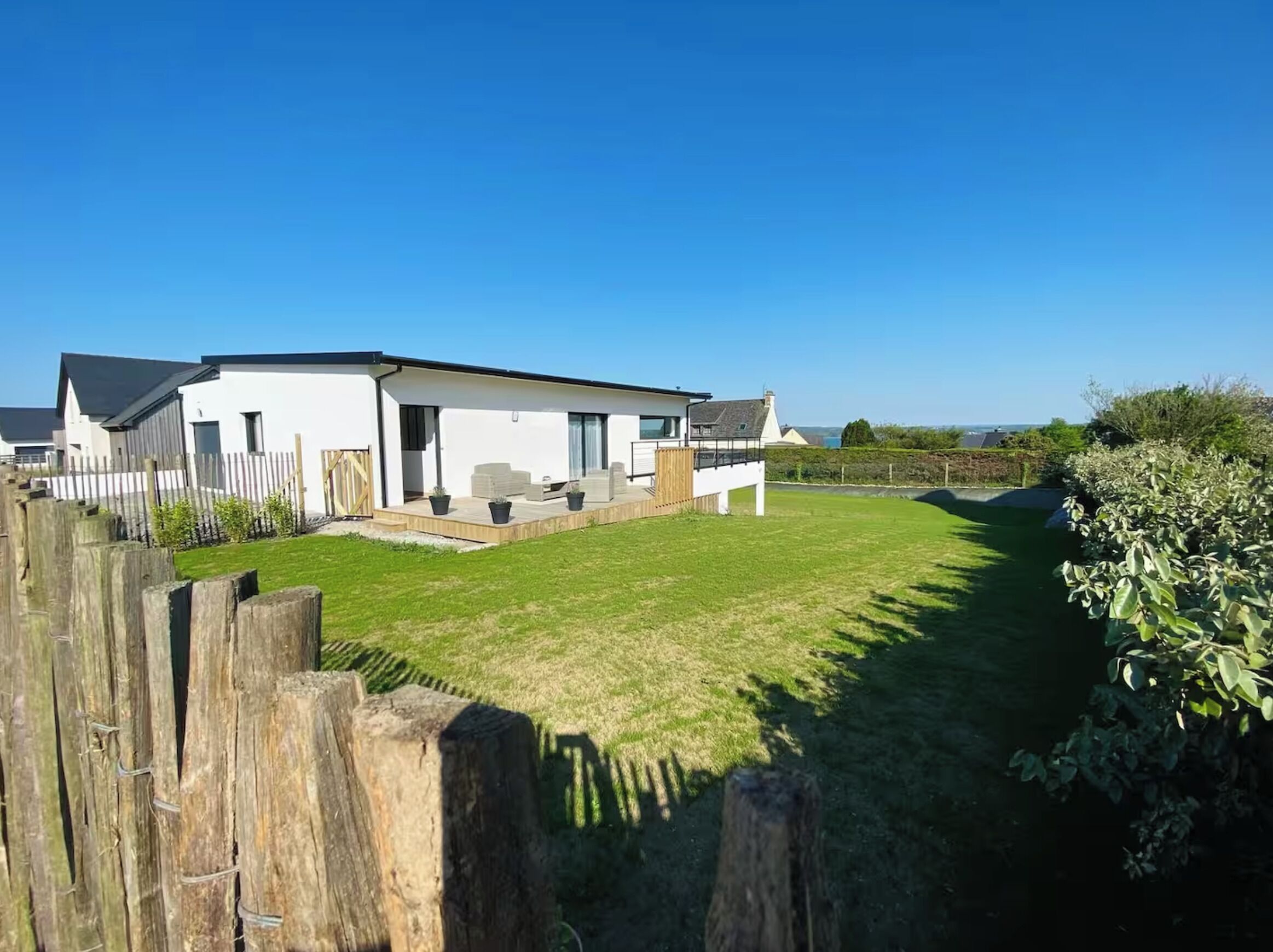 A modern single-story house with a covered patio, a fenced yard, and a view of the sea.