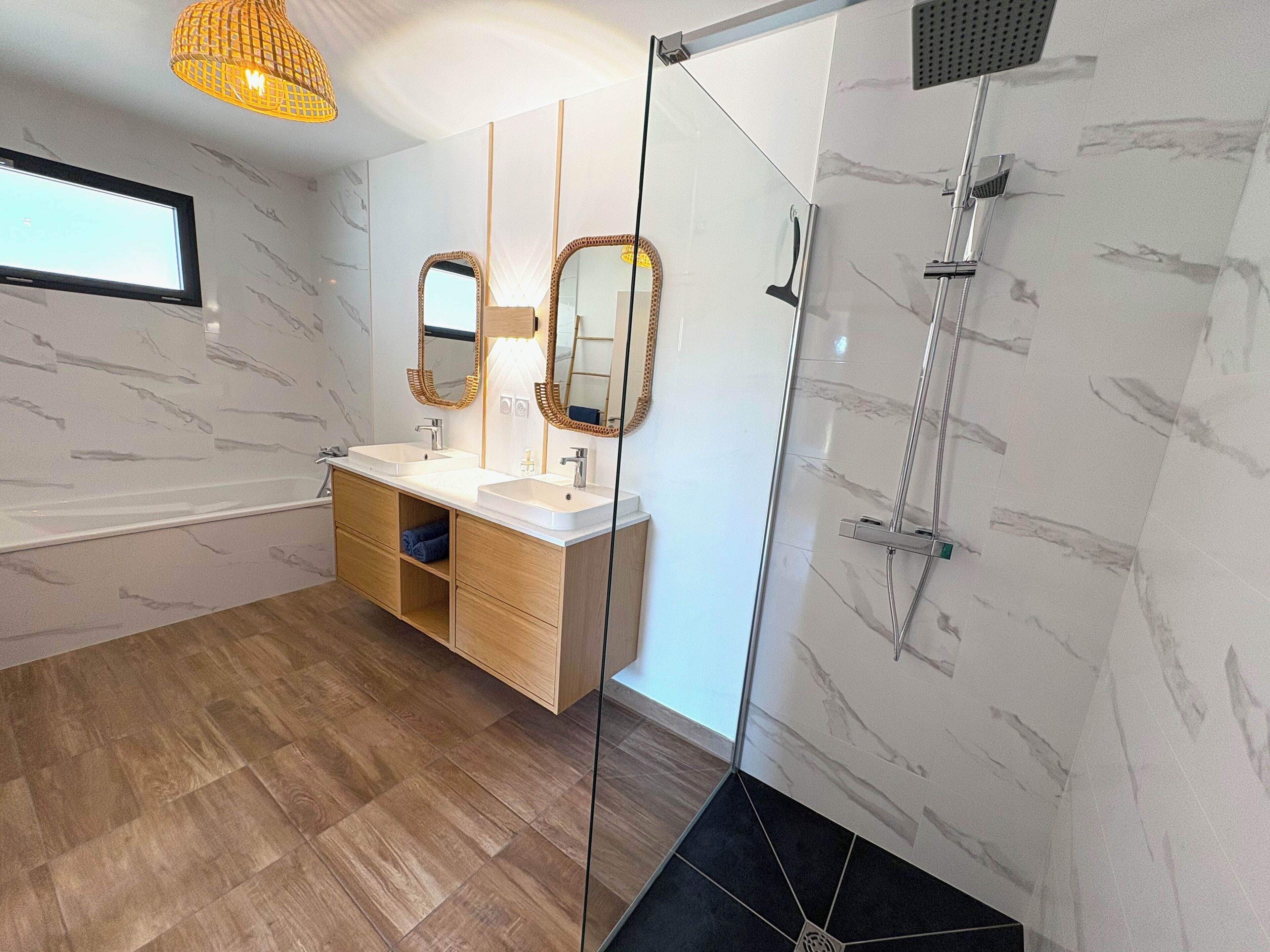 A modern bathroom with a glass shower enclosure, wooden vanity, and marble walls.