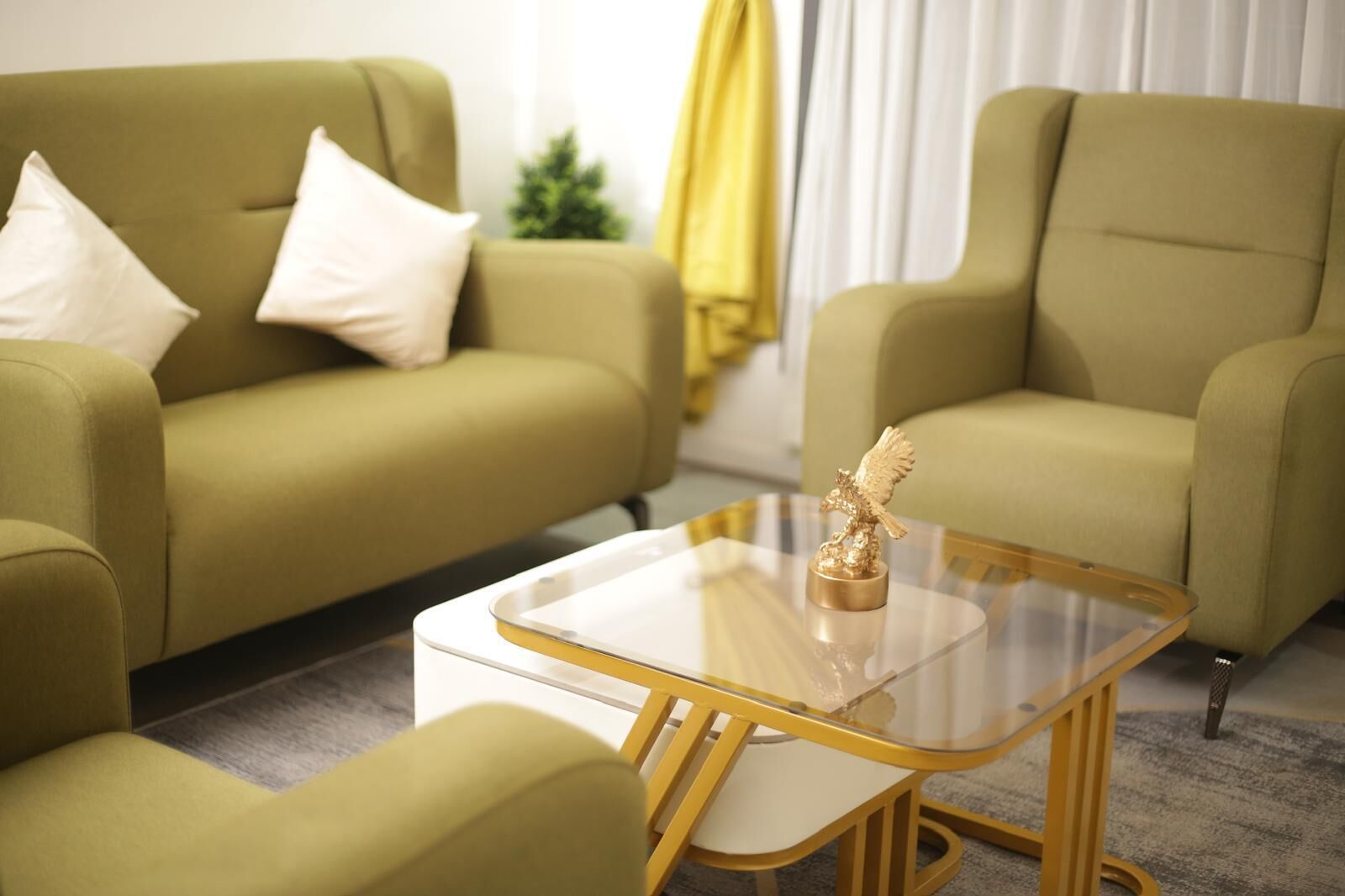Un salon moderne avec deux canapés verts, une table basse en verre dotée d’un pied doré et une petite statue dorée.