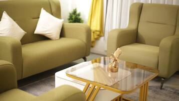 Un salon moderne avec deux canapés verts, une table basse en verre dotée d’un pied doré et une petite statue dorée.