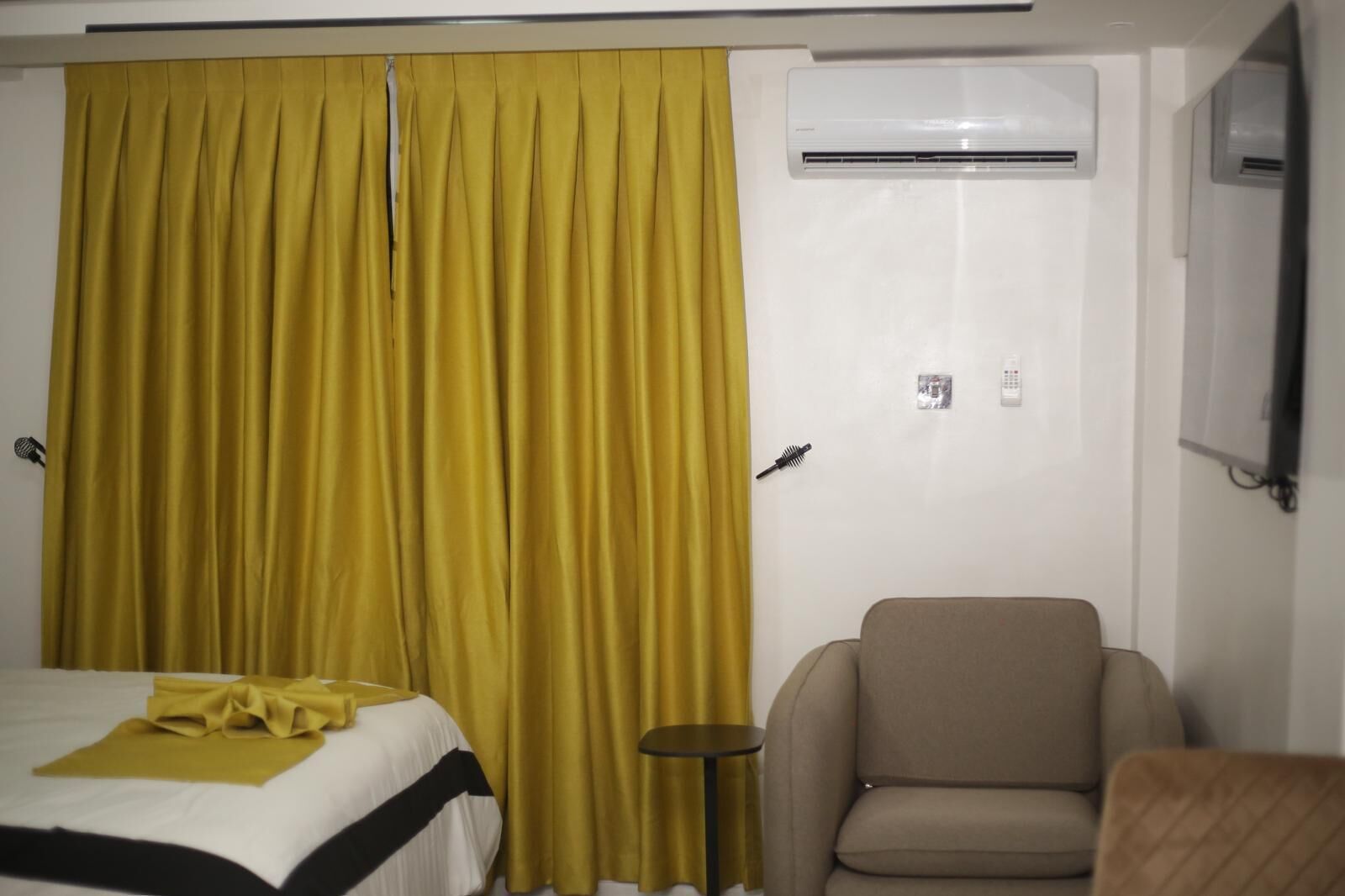 A hotel room with a bed, a chair, an air conditioning unit, and a curtain.
