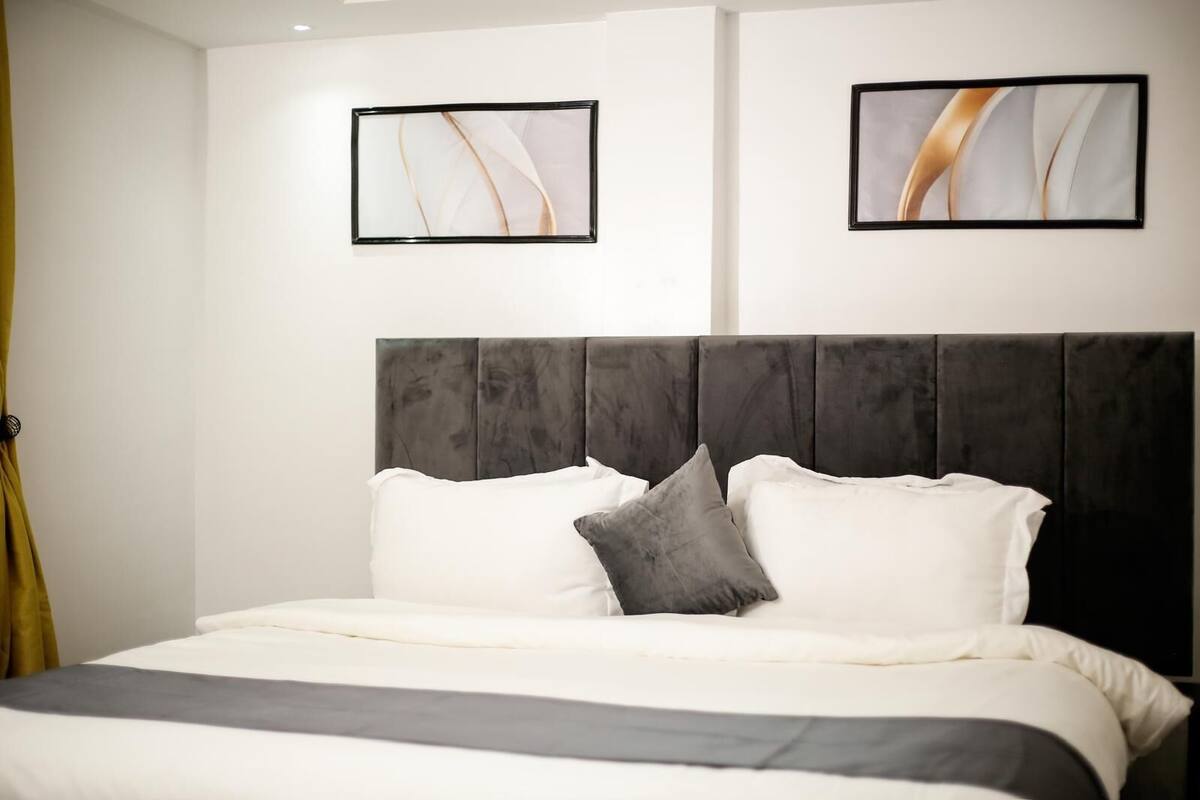 A bedroom with a large bed, a dark headboard, and two framed abstract paintings on the wall.