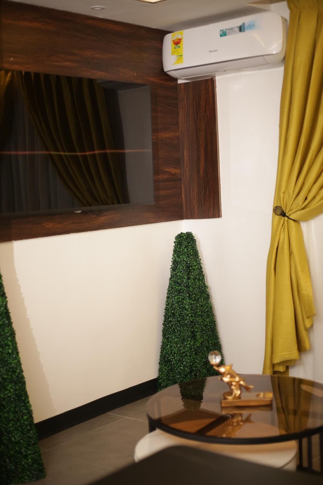 A modern room with a large window, a small potted plant, a glass table with a decorative item, and a ceiling-mounted air conditioner.