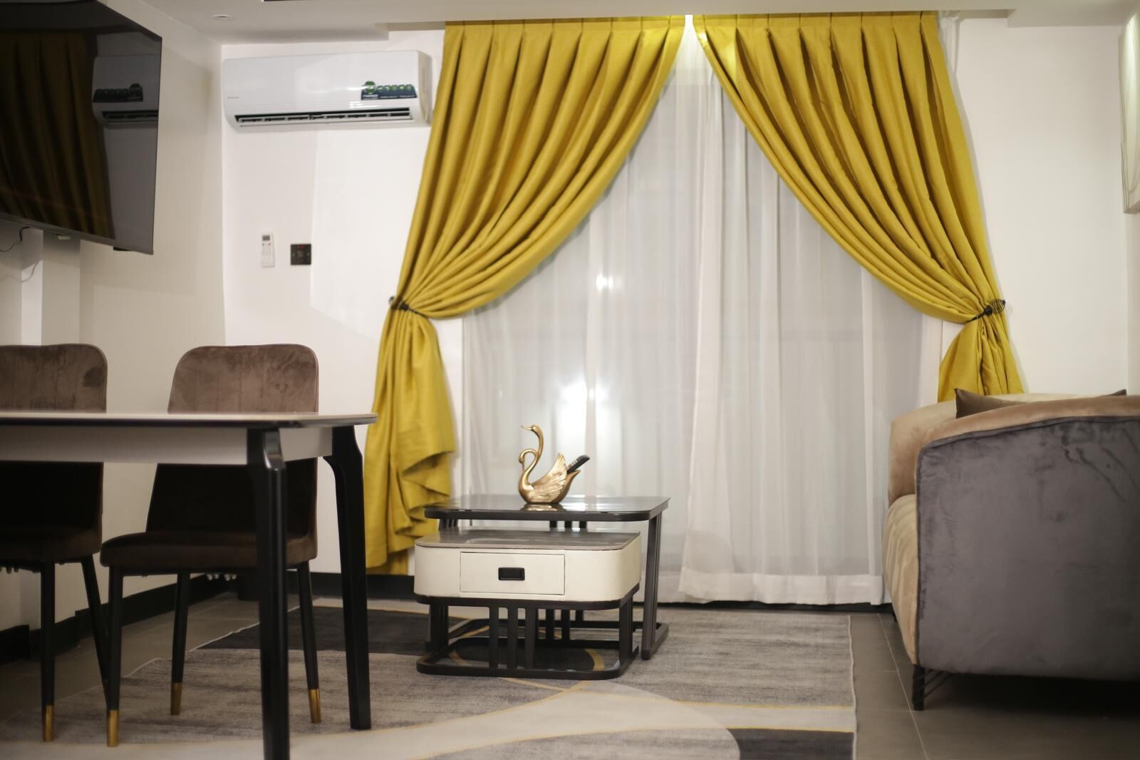Una habitación de hotel moderna con comedor, sofá y una cisne decorativa sobre la mesa.