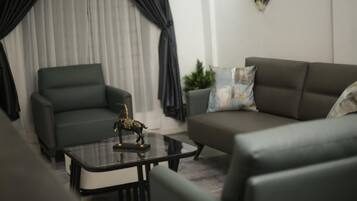 A modern living room with a dark green sofa, a matching armchair, and a glass coffee table with a decorative item.
