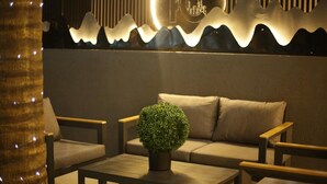 A modern lounge area with a sofa, two armchairs, and a coffee table. A decorative wall feature with a circular light and a cityscape logo is visible. - Kayla City (Kumasi)