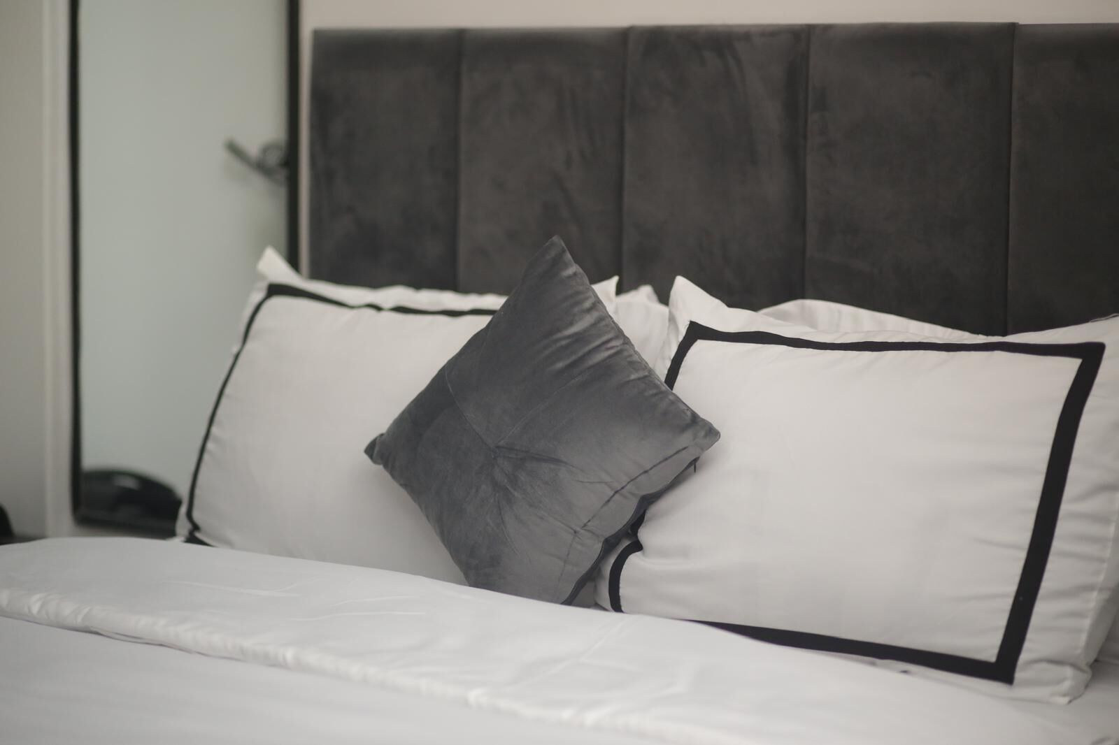 A bed with a dark headboard and white bedding, including pillows with black trim.