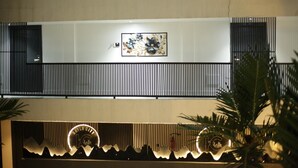 A multi-story building with a modern design, featuring a central framed artwork, a balcony with vertical slats, and a decorative light fixture at the entrance. - Kayla City (Kumasi)