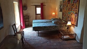 Habitació estreta amb un llit, una cadira, una taula i una làmpada.