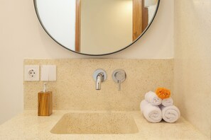 A bathroom with a round mirror, two wall-mounted faucets, a sink, a soap dispenser, and a stack of rolled towels. - 2BR Tropical Villa with Rooftop & Private Pool (cemagi)