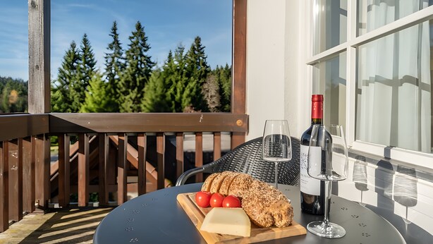 Ein Tisch mit einer Weinflasche, Gläsern, Käse und Tomaten auf einem Holzbruch.