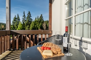 A table with a bottle of wine, glasses, cheese, and tomatoes on a wooden board.