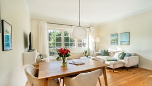 Ein modernes Wohnzimmer mit einem Holzesstisch, zwei Sofas, einem großen Fenster und einer hängenden Leuchte.