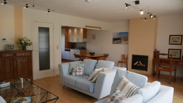 A living room with a light blue sofa, a glass coffee table, and a dining area with wooden furniture. - Dunette - Beautiful 3-bedroom villa with all comforts in the concession. (De Haan)