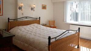 A bedroom with a bed, two wall-mounted lamps, a chair, and a window with blinds. - Dunette - Beautiful 3-bedroom villa with all comforts in the concession. (De Haan)