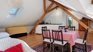 A loft-style bedroom with a skylight, a dining area with a red checkered tablecloth, and a kitchen area. - Studio 'Bergwiese' with Mountain View, Private Terrace and Private Garden (Lauterbach)