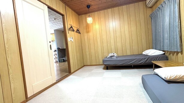 A room with wooden walls, a bed, a sofa, a hanging light fixture, and an air conditioning unit. - coco stay ishigaki (Ishigaki)