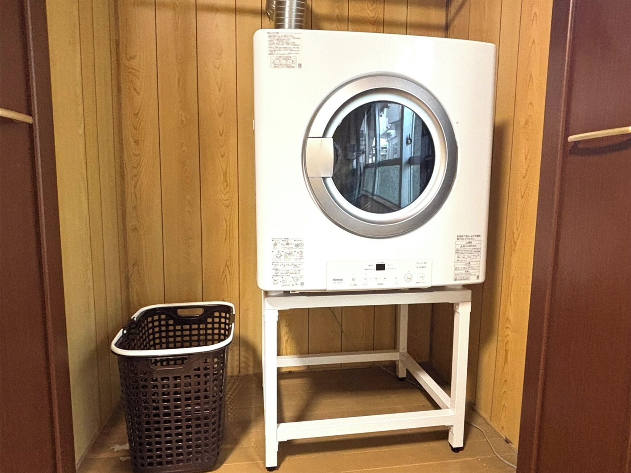 Une machine à laver blanche, posée sur un support blanc, dans une pièce aux murs en bois.