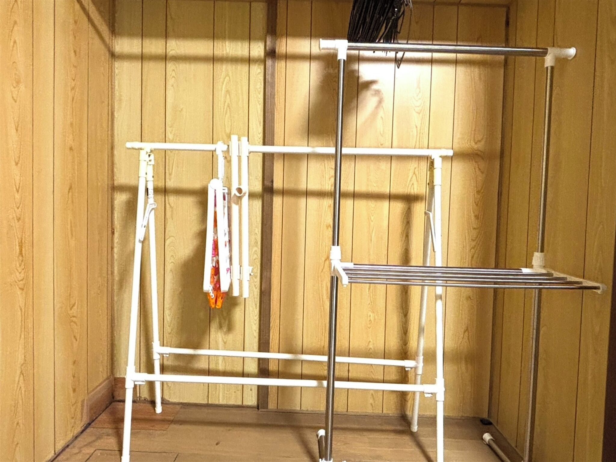 A metal drying rack with hooks and shelves against a wooden wall.