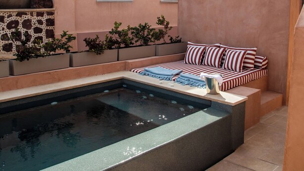 Zona de piscina con pared de piedra, un sofá con cojines a rayas y una ventana pequeña.