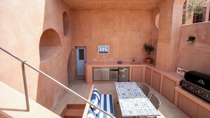 Un área de cocina al aire libre compacta con una mesa, sillas, una parrilla y una planta en maceta.